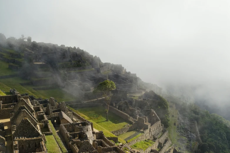 fog rises above the ruins at a village on top of a hill