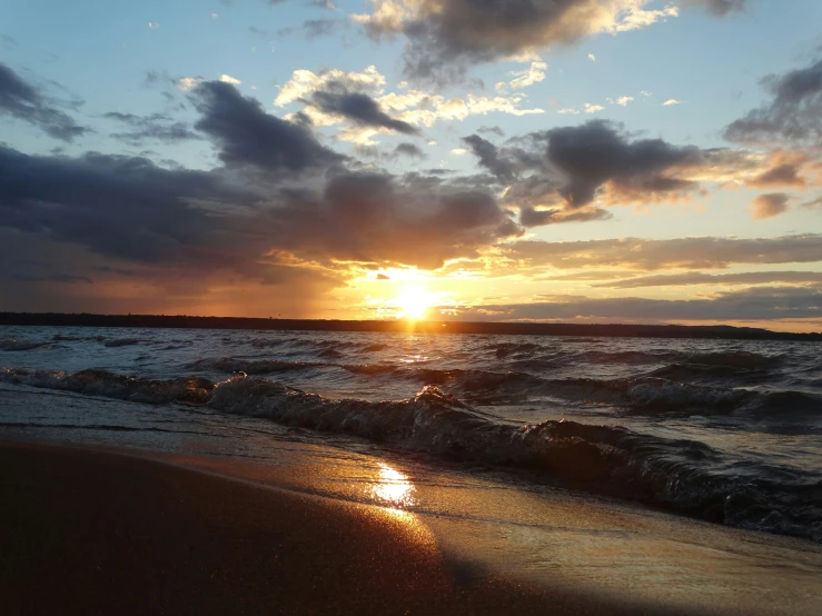 the sun setting over the ocean as the waves roll on the beach