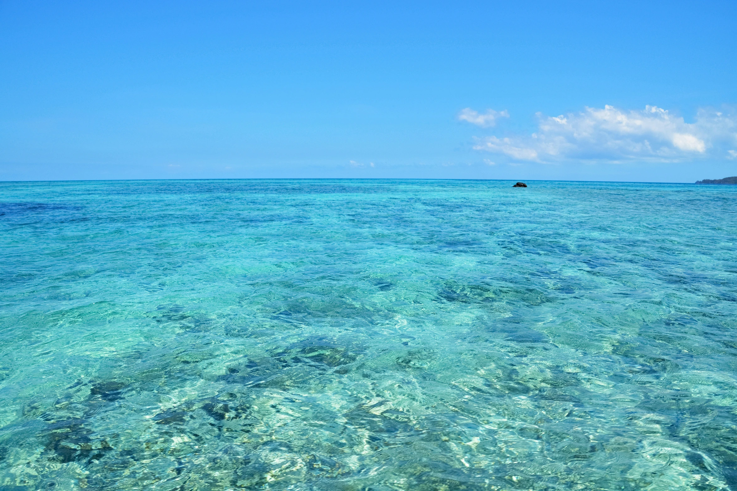 blue water at the beach with a lone boat in the distance