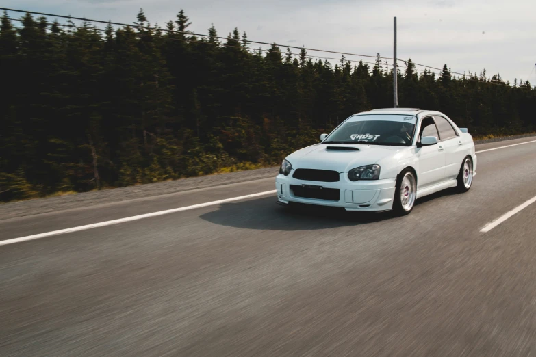 a white car driving on the road next to some trees