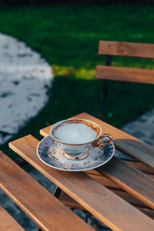 a cup with a saucer and plate sits on a wooden bench