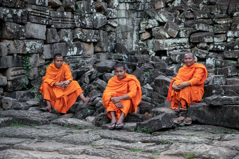 two male monks are sitting in a row on the rocks