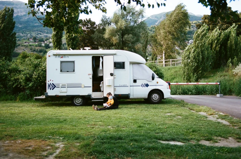 a woman sitting in the grass by a small trailer