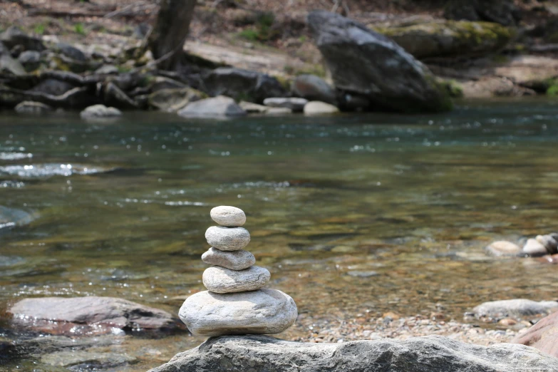 a rock stack next to water with a tree in the distance