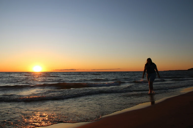 a person walking along the beach with the sun in the background