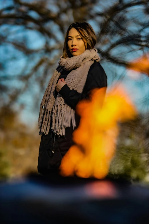 a woman wearing a scarf around her neck standing beside a bonfire