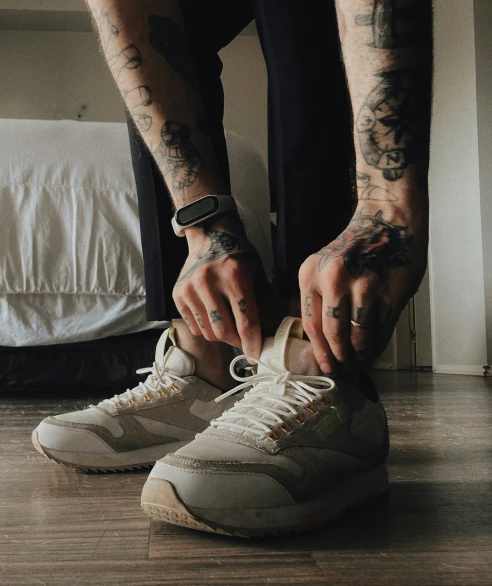 a tattooed man is tying his sneakers up