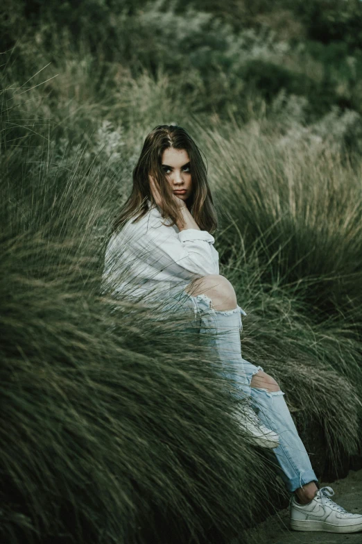 a girl sitting on top of tall grass next to bushes