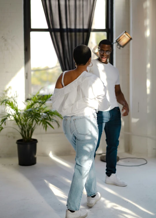 two people in jeans and white shirts in a room with a window