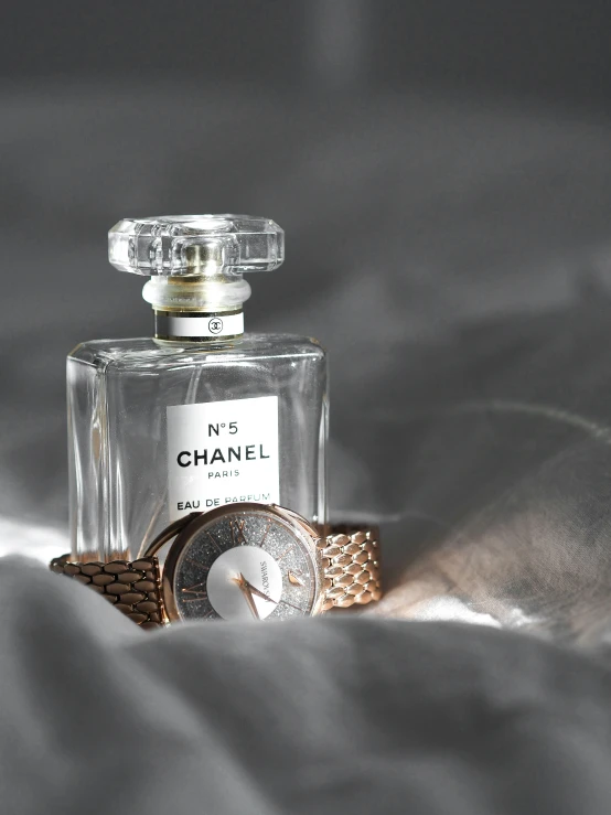 a small perfume bottle with a watch beside it