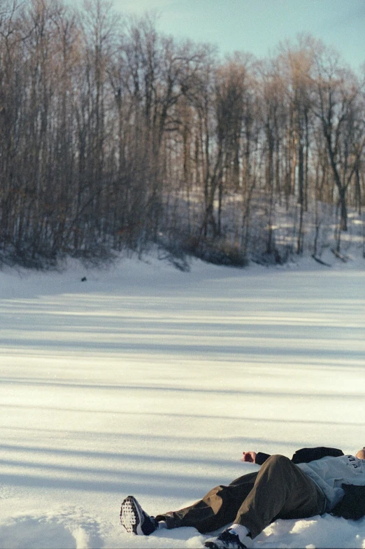 a person laying in the snow on their stomach with the end of a sled