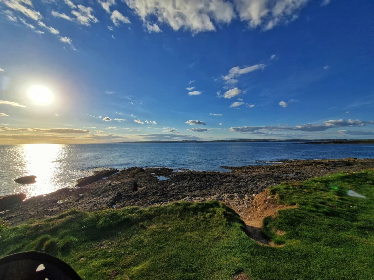 sun shining above green field and body of water