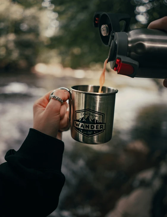 someone pouring coffee into a metal cup with the handle down