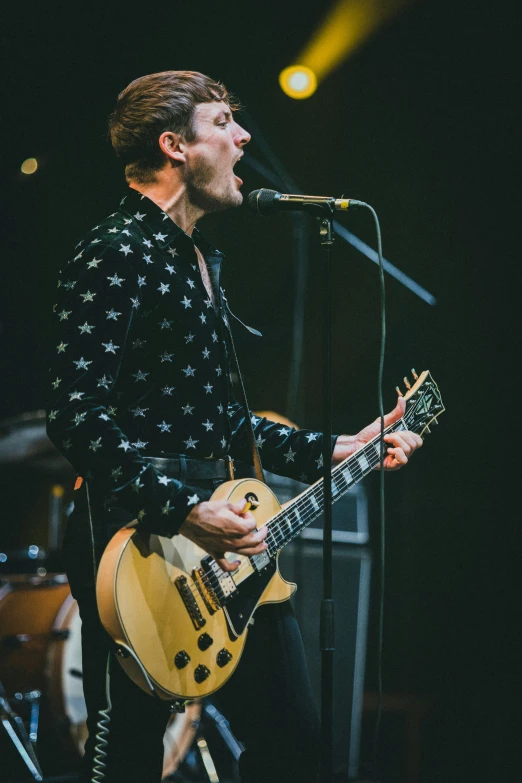 man singing into microphone while holding a guitar