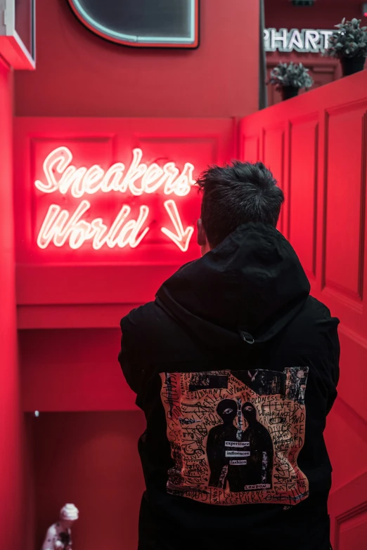 a man with a black hoodie stares at a neon sign