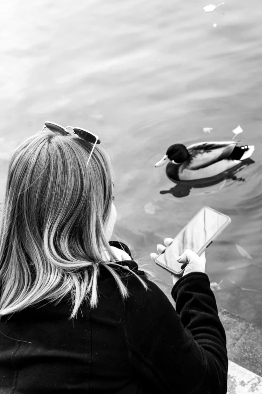 a young woman is sitting by a pond with her duck