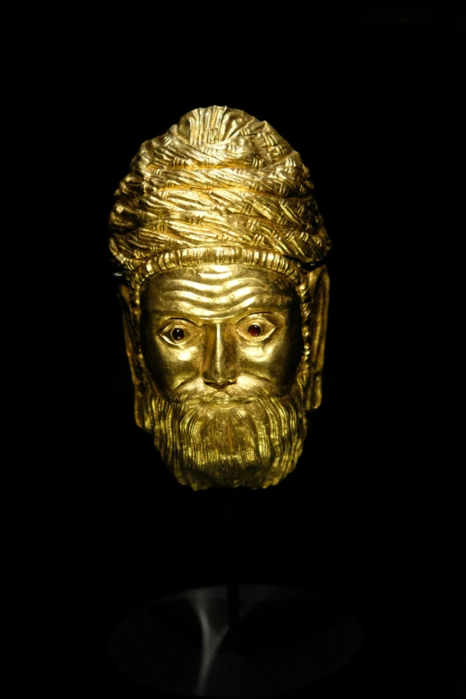 golden face sculpture is pographed against a black background
