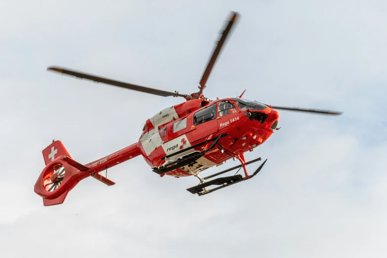 a red helicopter flying through the sky on a cloudy day