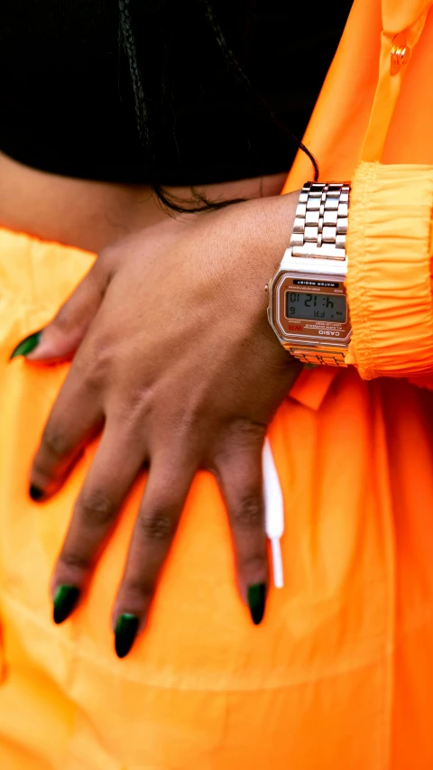 an orange dress with green nails in front of an arm and a watch