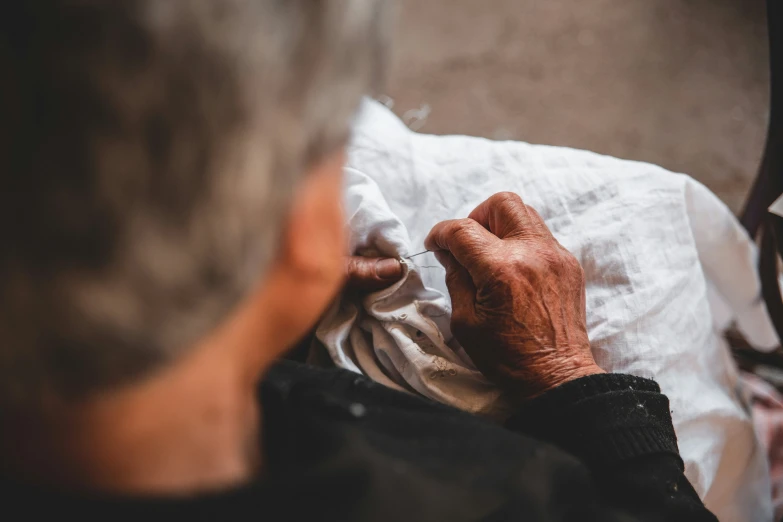 an elderly person sitting on a chair sewing soing