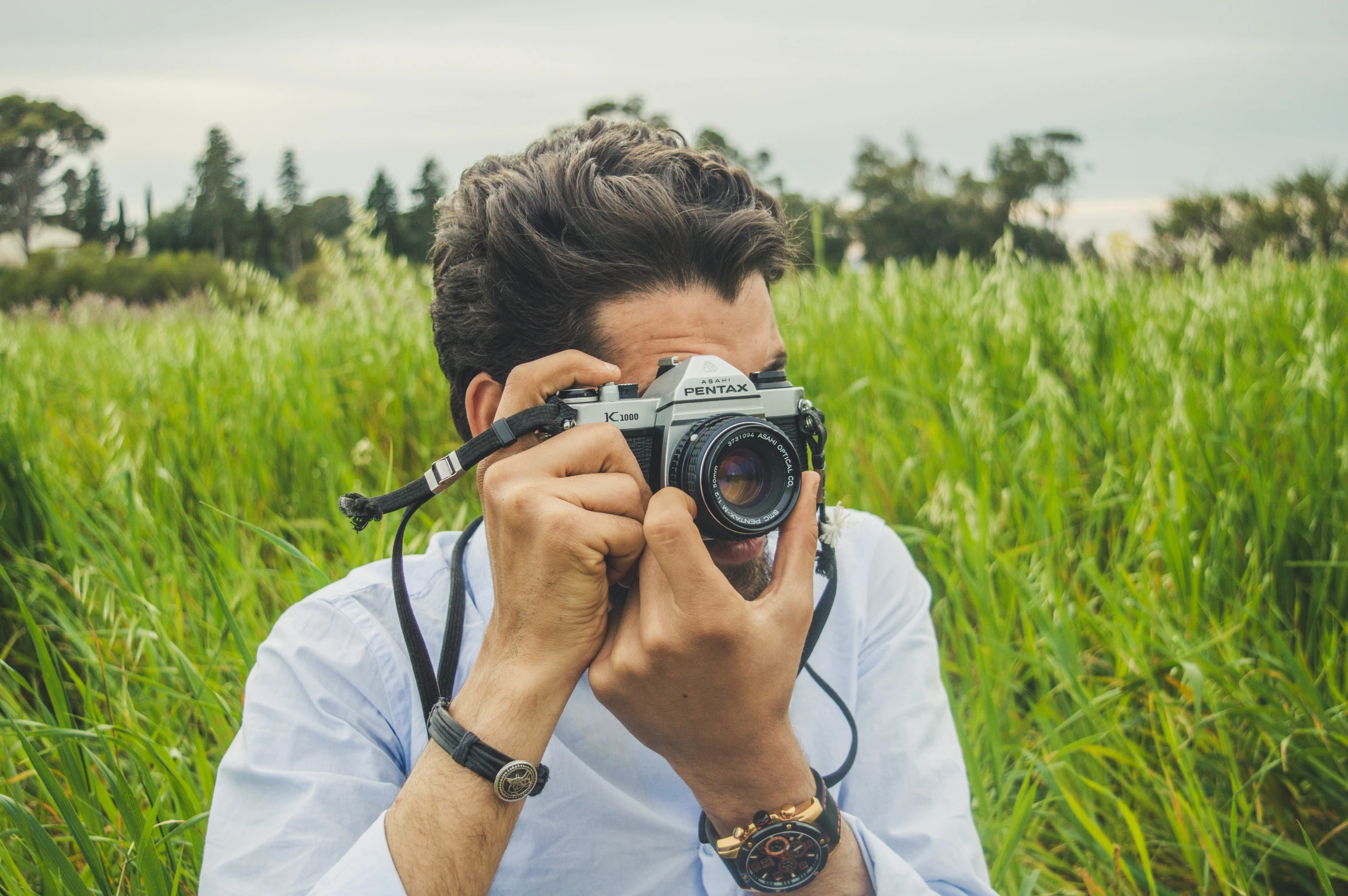 a young man in a white shirt holding a camera up to his face while wearing a white collar shirt