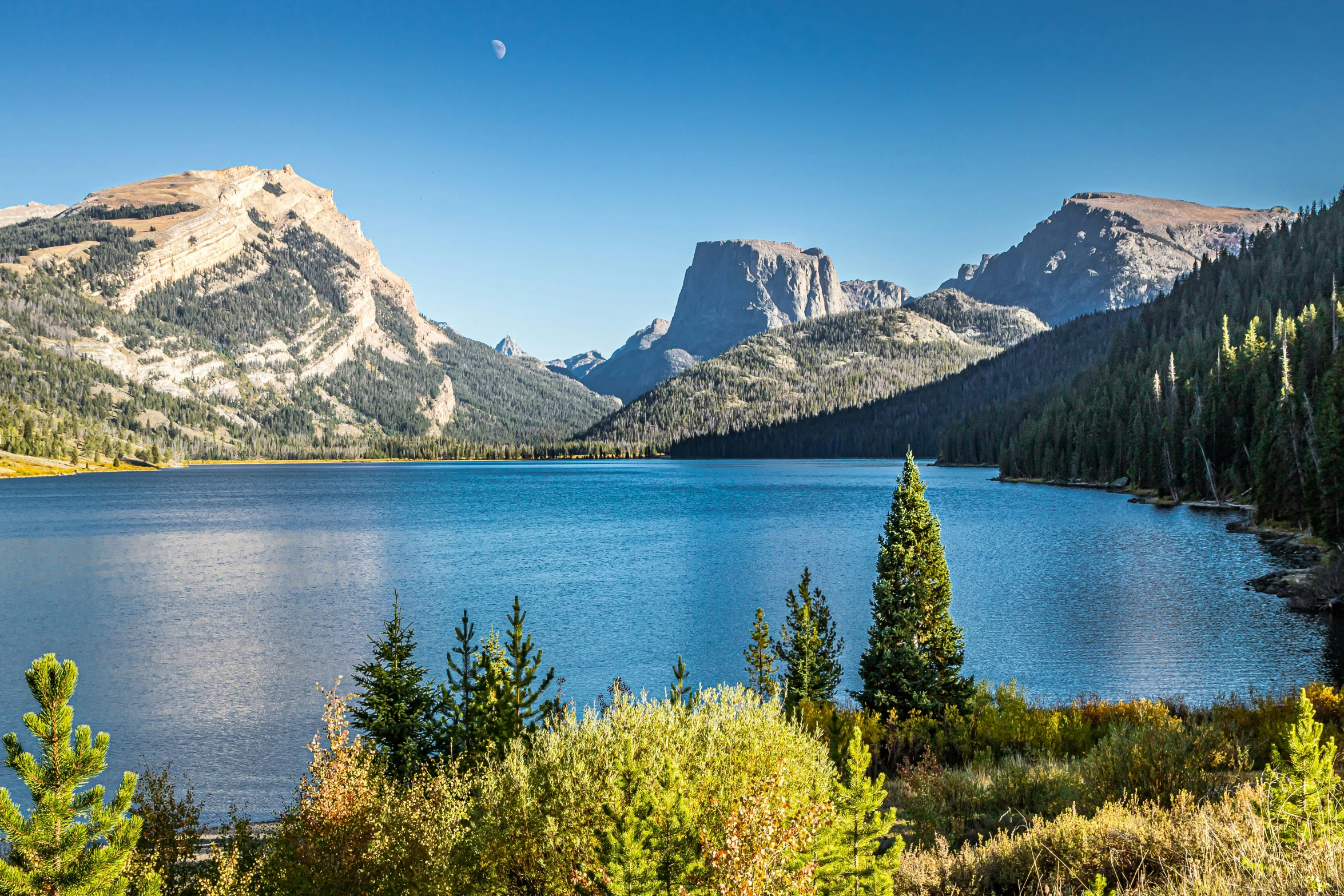 a lake with blue water surrounded by trees and mountains