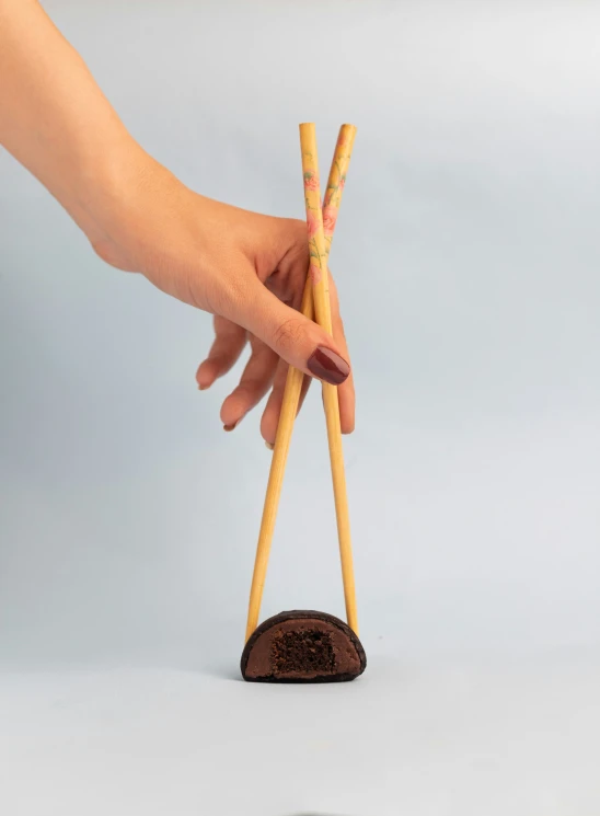 a hand holding two chop sticks over a miniature coin