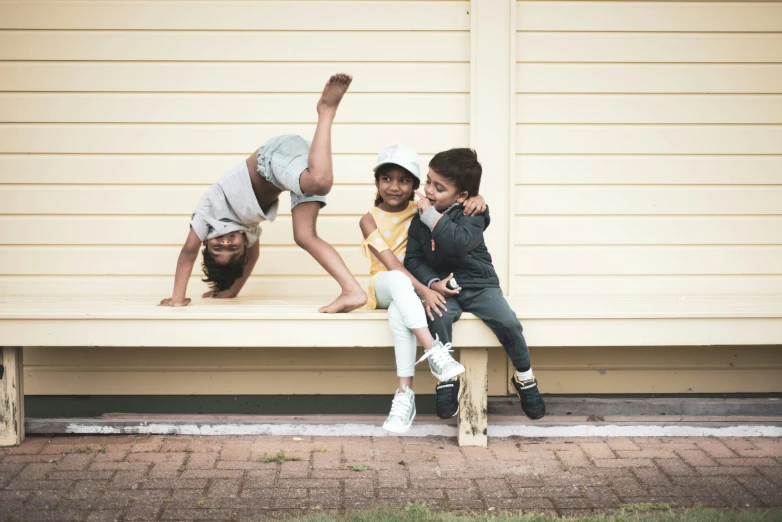 three children are sitting on a bench with their hands raised up