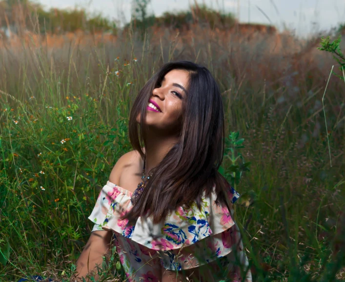 a woman sitting in the grass smiling and making funny faces