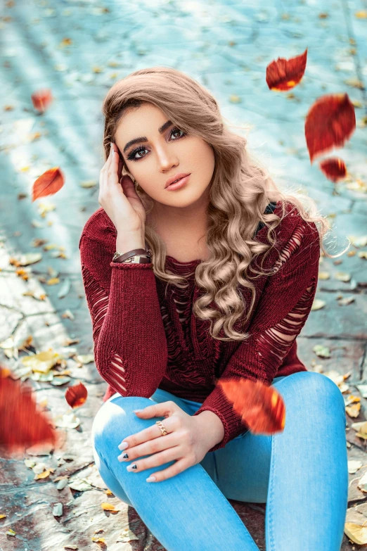 a pretty young woman sitting on top of a leaf covered ground