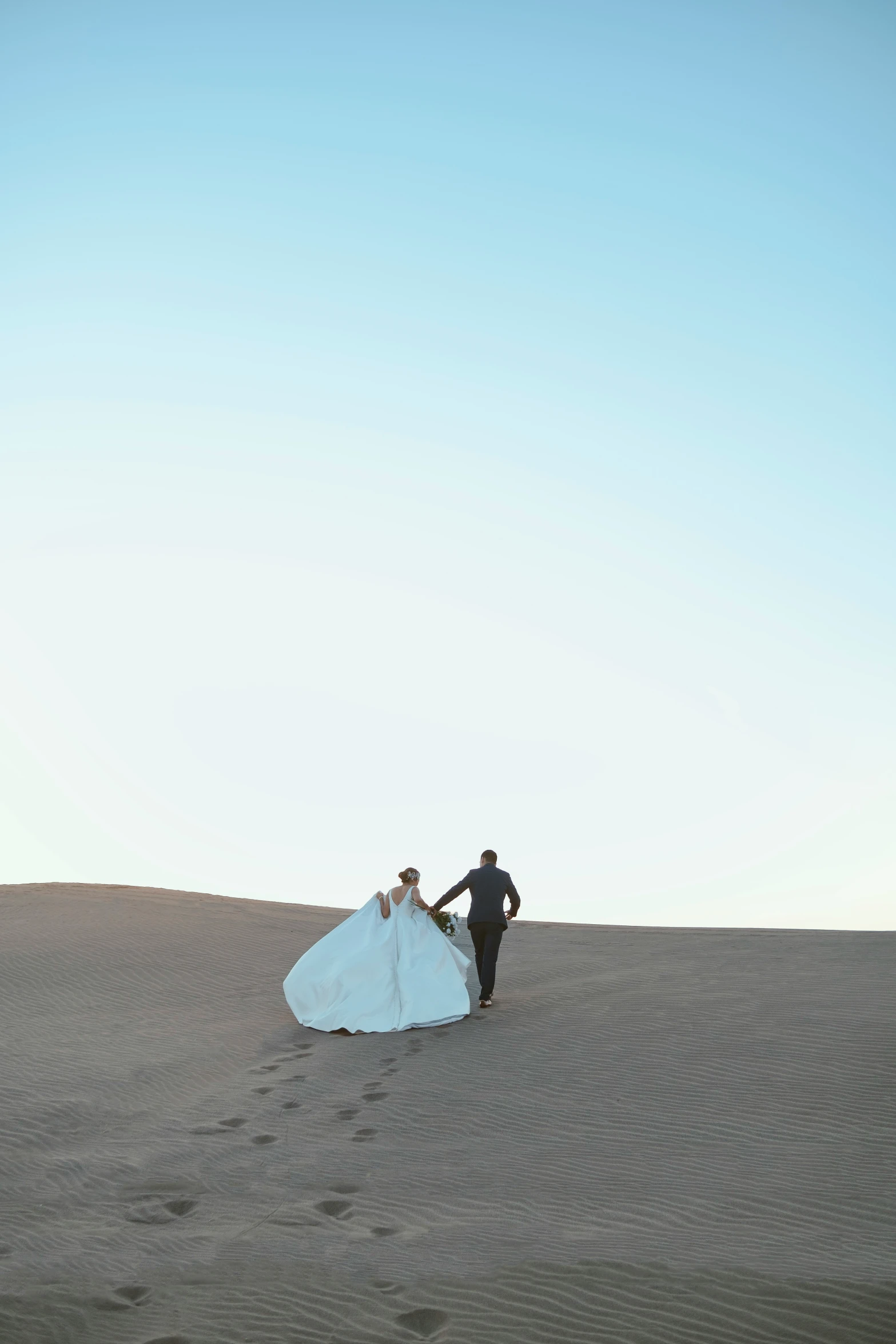 the bride is carrying her gown while walking in the sand