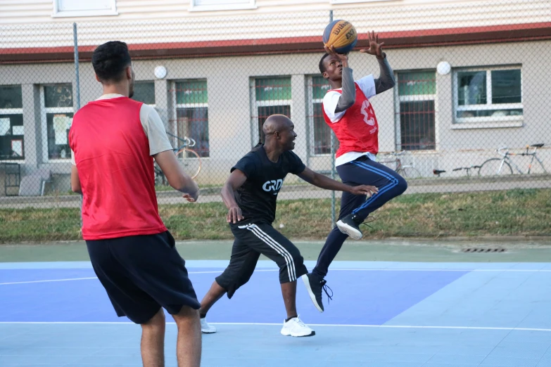 three young men standing on a tennis court playing basketball