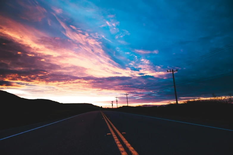 the sun sets behind a hill and a long street