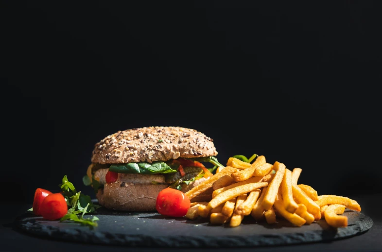 a sandwich, french fries and tomatoes are laid out on a black surface