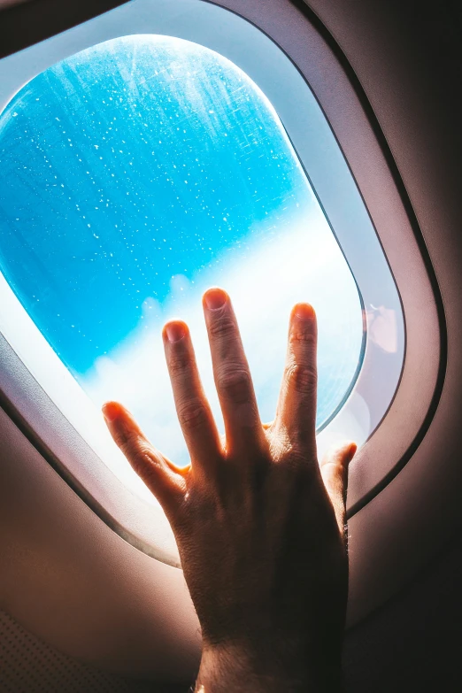 a hand touching a blue wing window during flight