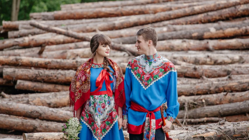 a man and woman standing next to each other near a pile of logs