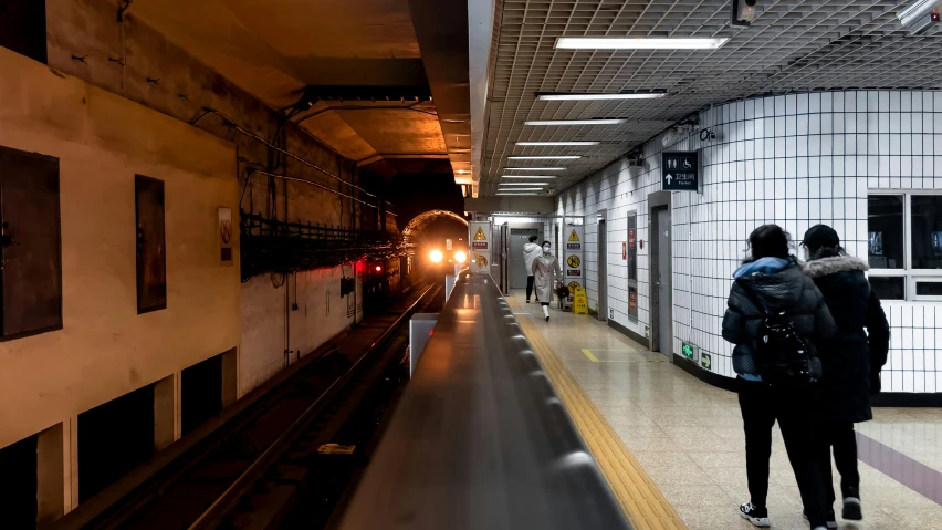 two people standing on a platform watching a train coming down the track