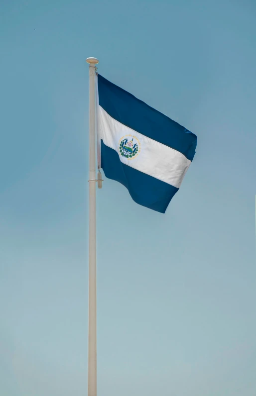 flag waving high in a blue sky near the water