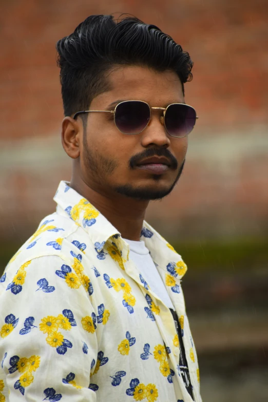 a man with sunglasses on, standing in front of a brick wall