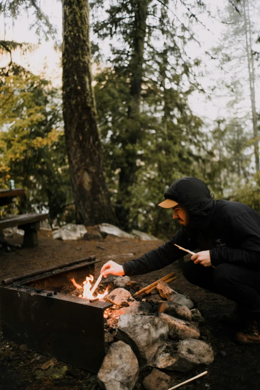 a person in a hooded jacket is lighting a bonfire