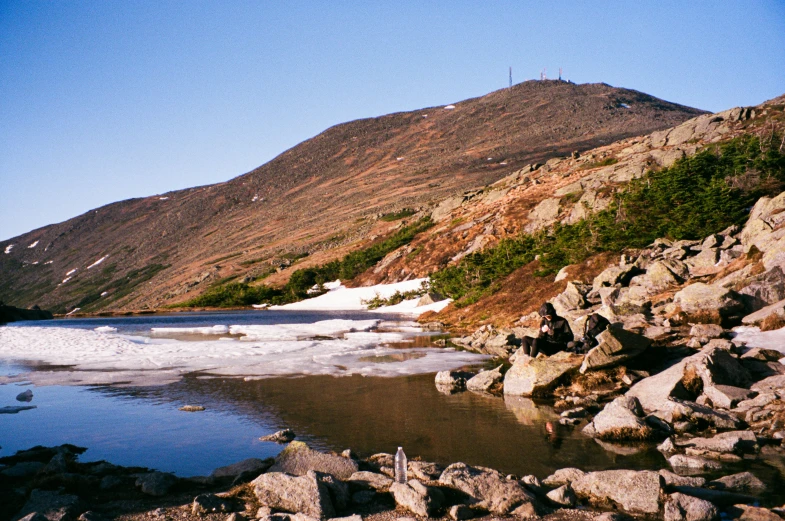 a large pile of rocks near water in the mountains
