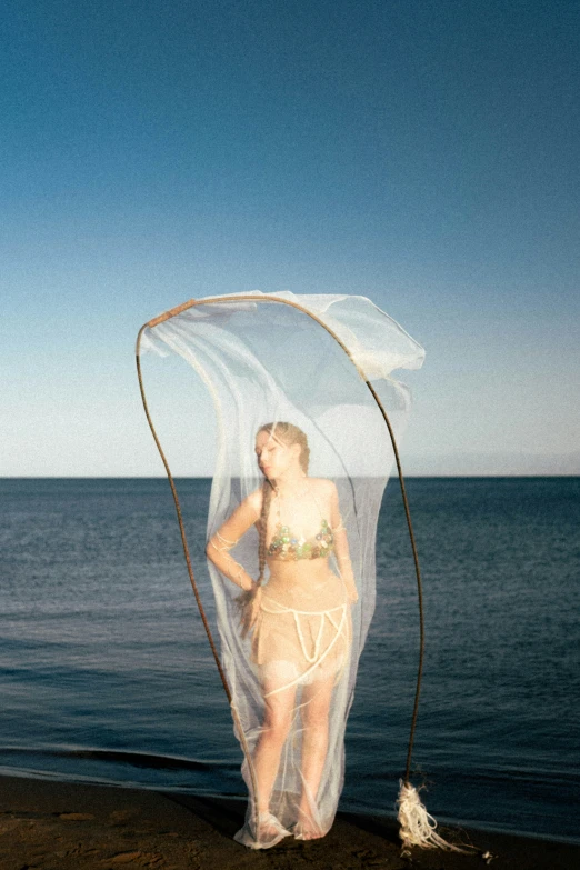 a woman dressed in swimsuit posing on a beach next to the ocean