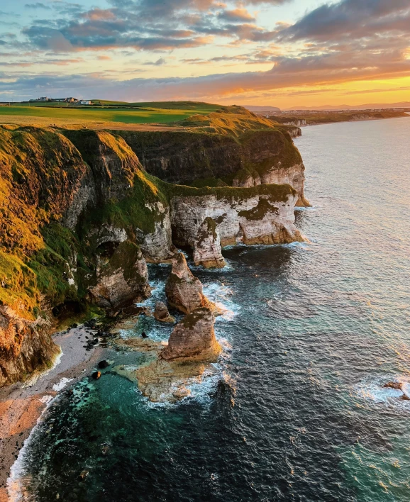 a scenic view of the sea, rocks and grass at sunset