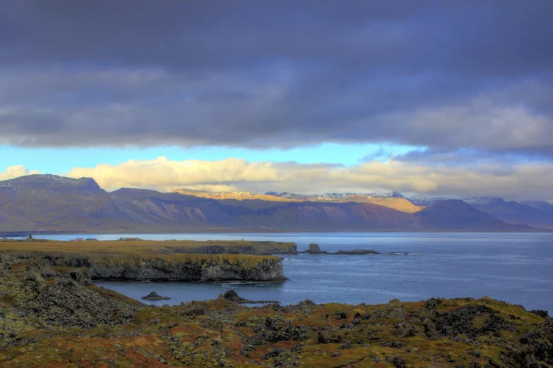 an island surrounded by mountains under cloudy skies