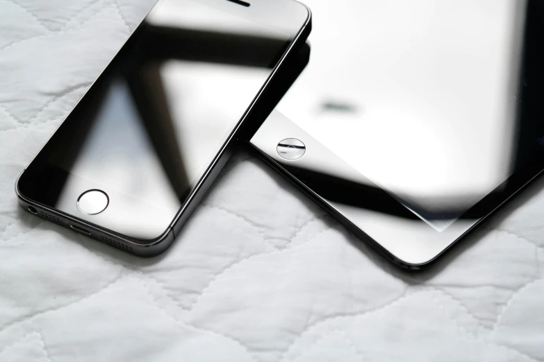 a pair of black cellular phones laying on a white blanket