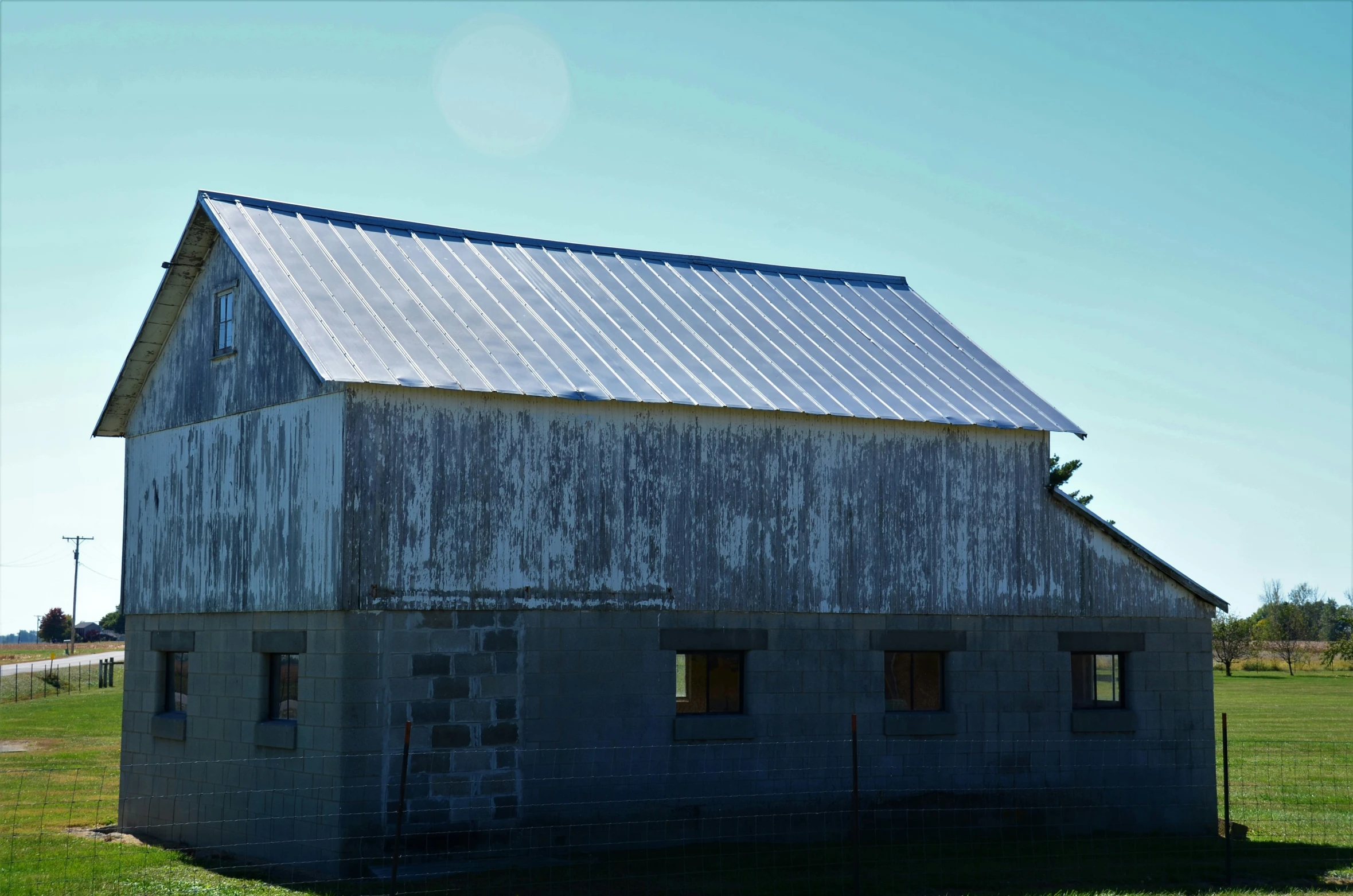 an old weathered, gray barn sits in a grassy field