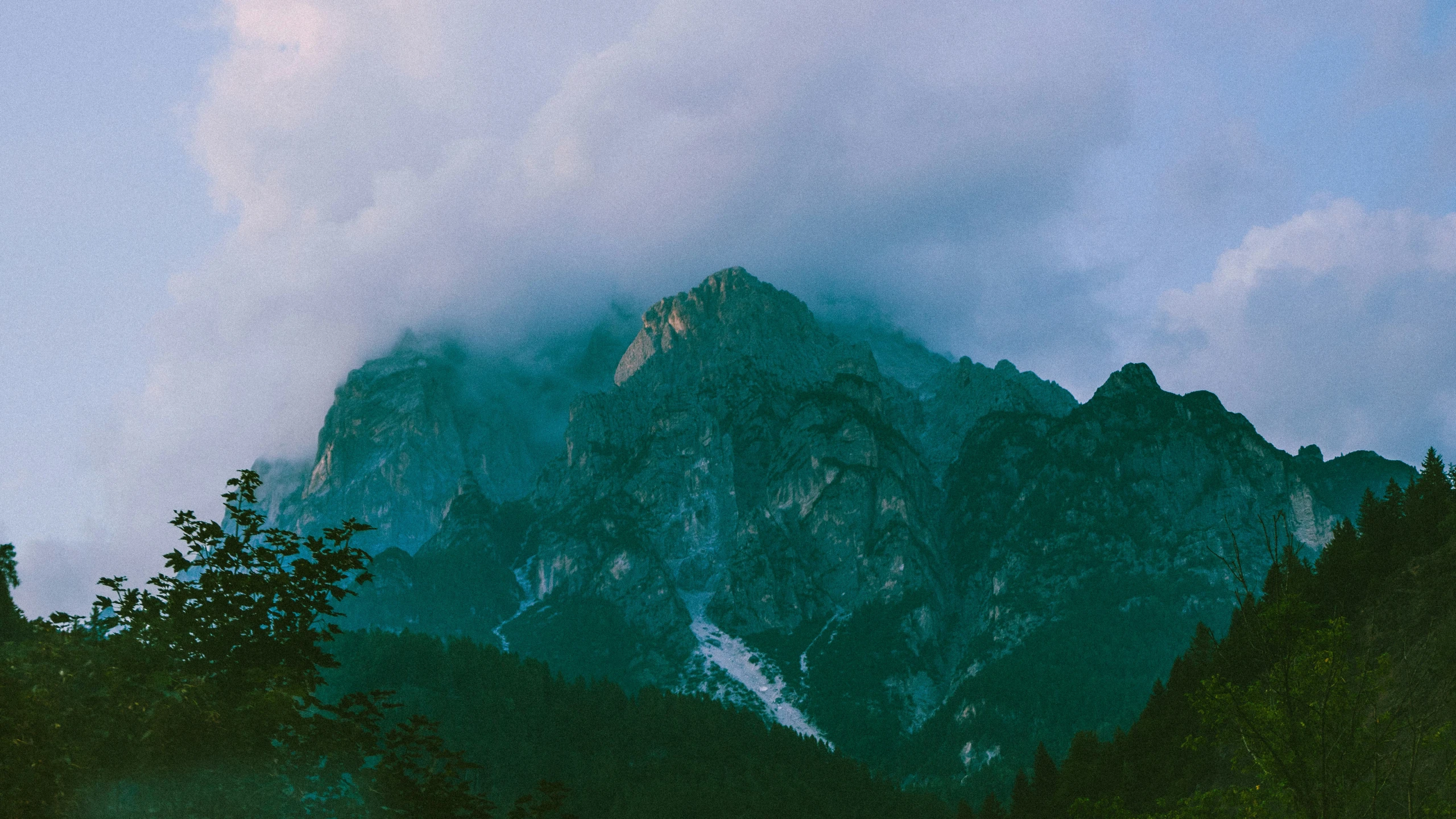 green trees on the side of a mountain under a blue sky with clouds