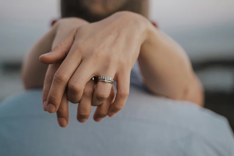 two women are holding hands, one is wearing a engagement ring