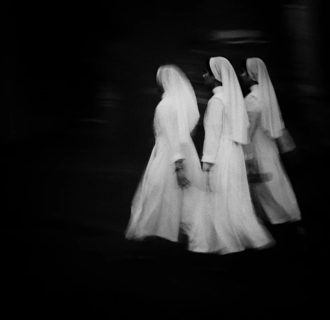 three women dressed in white robes walk together