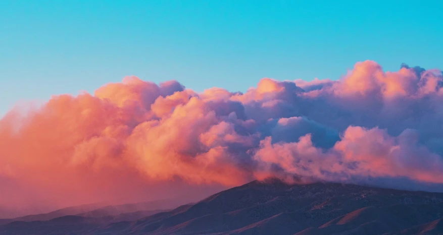 a mountain with many clouds and a plane flying above it